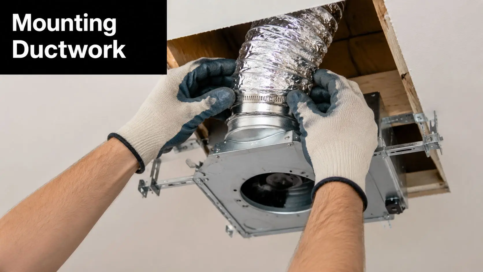 A professional installer connecting flexible aluminum ductwork to a bathroom exhaust fan housing in the ceiling.